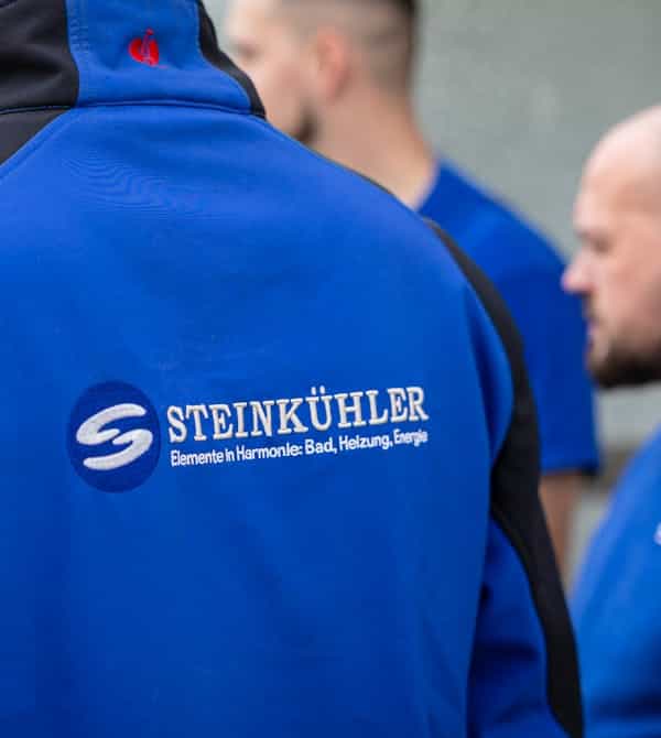 Mehrere Mitarbeiter eines Fachbetriebs stehen im Austausch, während sie Arbeitskleidung mit Firmenlogo tragen; die Szene zeigt Teamarbeit, Professionalität und den Einsatz im Bereich moderner Haustechnik – Steinkühler Wasser & Wärme GmbH & Co. KG