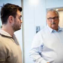 Ein erfahrener Mitarbeiter hört aufmerksam den Anliegen eines Kunden zu, während ein Kollege im Hintergrund das Gespräch begleitet; die Szene zeigt persönliche Beratung, Vertrauen und kundenorientierten Service im Bereich moderner Haustechnik – Steinkühler Wasser & Wärme GmbH & Co. KG