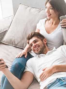 Paar sitzt gemeinsam auf dem Sofa und freut sich über das Licht und Steuerung System von Steinkühler in Leverkusen.